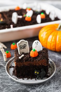 a piece of chocolate cake on a plate with halloween decorations around it and two pumpkins in the background