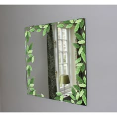 a mirror with green leaves on it and a lamp in the corner next to it