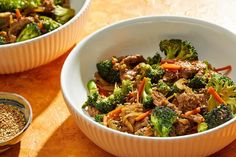 two bowls filled with meat and broccoli on top of a wooden table next to seasoning