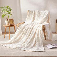 a white blanket sitting on top of a chair next to a wooden table and potted plant