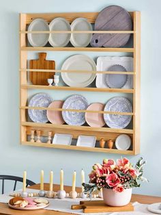 a wooden shelf filled with plates and flowers on top of a dining room table next to a candle holder