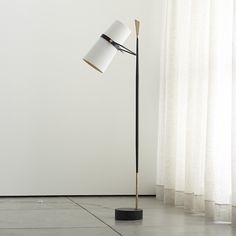 a floor lamp with a white shade on it and a black base in front of a window