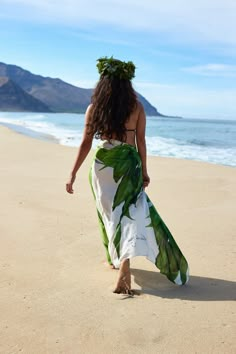 a woman walking on the beach wearing a green and white dress with flowers in her hair