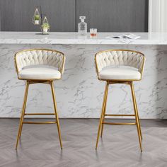 two white and gold bar stools sitting in front of a marble counter