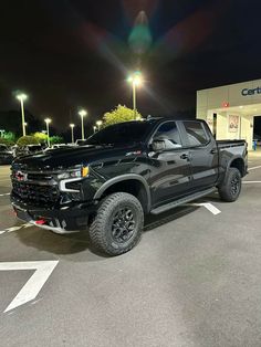 a black truck is parked in a parking lot at night with its lights turned on