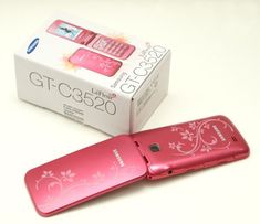 a pink cell phone sitting on top of a white table next to a boxed box