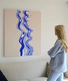 a woman standing in front of a painting on the wall next to a white couch