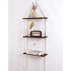 three tiered shelf with books, vase and other items on it against a white wall