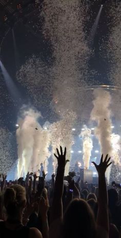 the crowd is watching fireworks go off in the night sky at a concert with their hands up