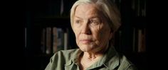 an older woman with white hair and green shirt sitting in front of bookshelves