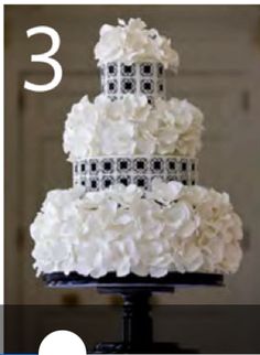 a three tiered wedding cake with white flowers on the top and black trimmings