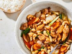 a white bowl filled with meat and vegetables next to rice on top of a table