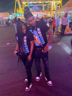 a man and woman standing in front of an amusement park at night with neon lights