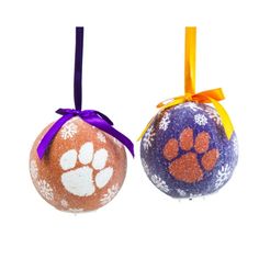 two ornaments with paw prints on them are hanging from purple and orange ribbons, one has an orange bow