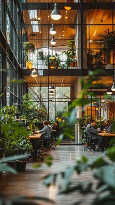 people sitting at tables in an office building with plants on the walls and windows above them