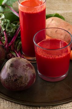 two glasses of beet juice next to some vegetables