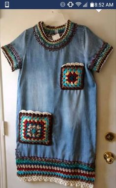 a blue dress with crocheted patches on the front and back, hanging up against a wall