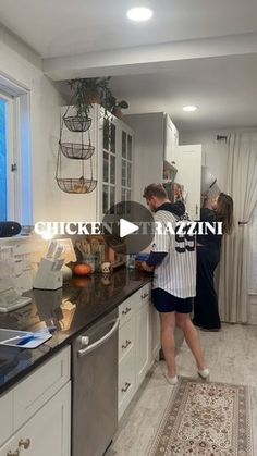 two people standing in a kitchen preparing food on the counter and looking out the window