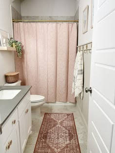 a bathroom with a pink shower curtain and rug on the floor next to the toilet