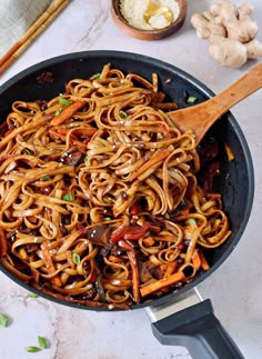 a skillet filled with noodles and vegetables next to chopsticks on a table