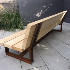 a wooden bench sitting on top of a stone floor next to a planter filled with grass