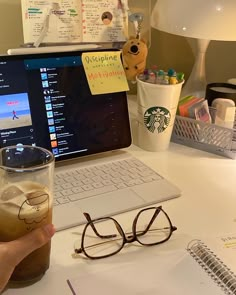 a laptop computer sitting on top of a desk next to a cup filled with liquid