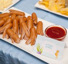 hot dogs on a plate with ketchup and chips next to it at a baby shower