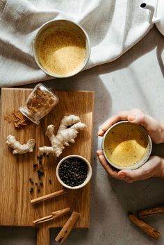 a person holding a bowl with some food in it on a wooden cutting board next to two mugs