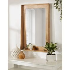 a wooden mirror sitting on top of a white table next to a potted plant