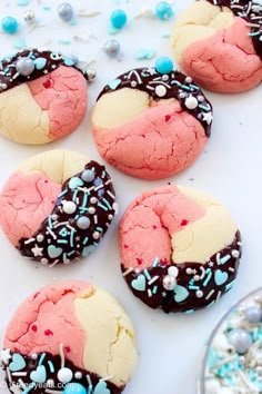 several cookies with sprinkles and frosting are on a white surface next to blue and white candies