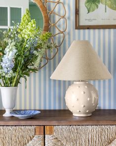 a white vase sitting on top of a wooden table next to a lamp and mirror