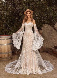 a woman in a wedding dress standing next to a barrel and wearing a cowboy hat