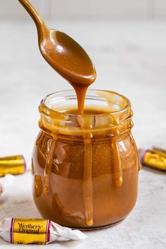 a spoon full of caramel sauce being poured into a jar