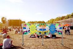 a group of people sitting on top of a field next to a colorful sign with words