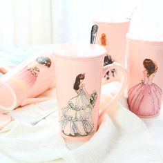 three coffee mugs with designs on them sitting on a white table cloth next to utensils