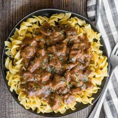 a bowl filled with pasta and meat sauce on top of a wooden table next to a fork