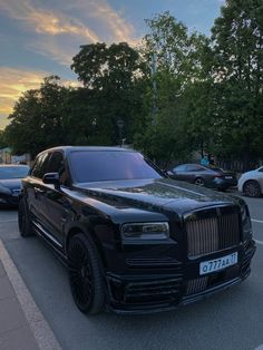 a black rolls royce parked on the side of a road next to other cars and trees