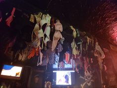 there are many bras hanging from the ceiling in this bar with neon lights behind them