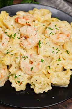 pasta with shrimp and cream sauce in a black plate on a wooden table next to parsley