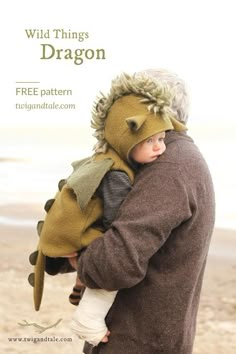 a man holding a child in his arms while wearing a dragon costume on the beach