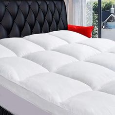 a white bed with black headboard and red pillows on it in a room next to a window