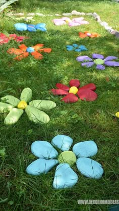 colorfully painted flowers are in the grass near rocks and stones that look like they have been made out of paper machs