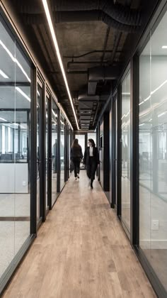 two people walking down a hallway in an office building with glass walls and wood flooring