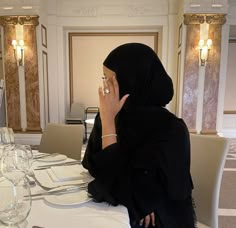 a woman wearing a hijab sitting at a table talking on her cell phone