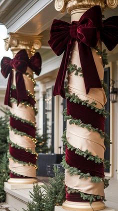 two tall christmas trees are decorated with bows and garlands on the pillars in front of a house