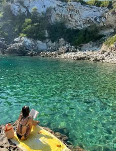 a woman sitting on top of a yellow kayak in the water next to rocks