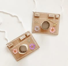 two small cameras with flowers on them are sitting next to each other, one is brown and the other is pink