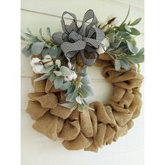 a burlock wreath with cotton and greenery on the front door, hanging from a wall