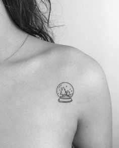 a black and white photo of a woman's shoulder with a snow globe tattoo on it