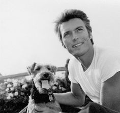 a black and white photo of a man holding a dog on his lap with flowers in the background